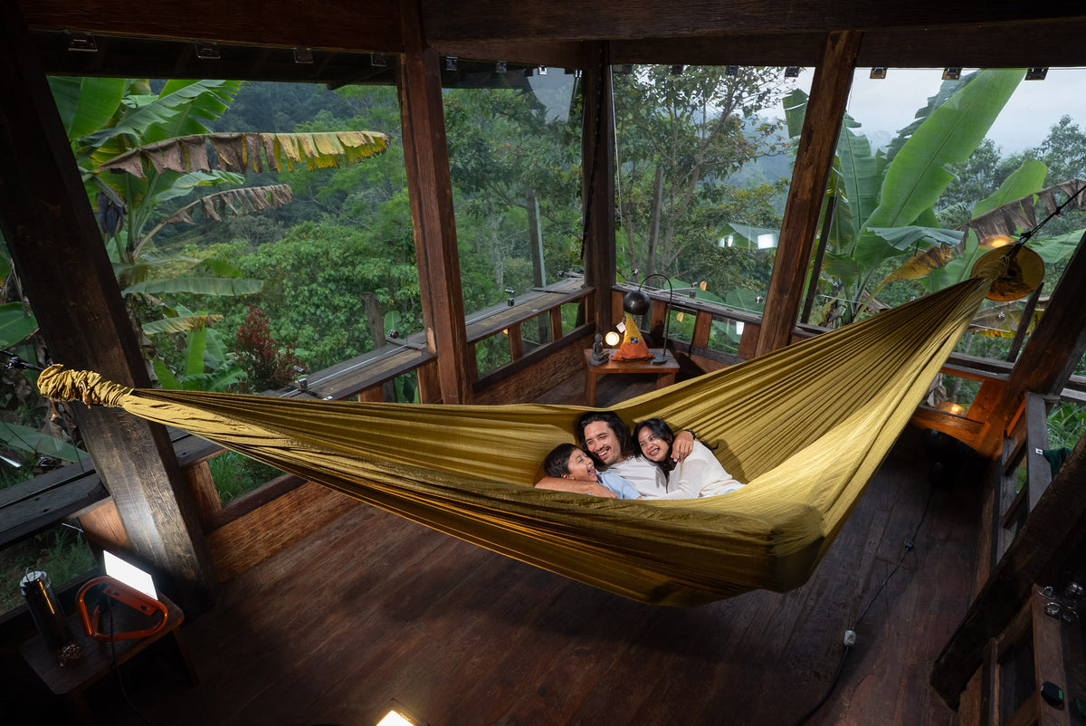 Dreiköpfige Familie liegt nebeneinander in einer goldenen Home Hammock 520 in einem offenen Holzpavillon