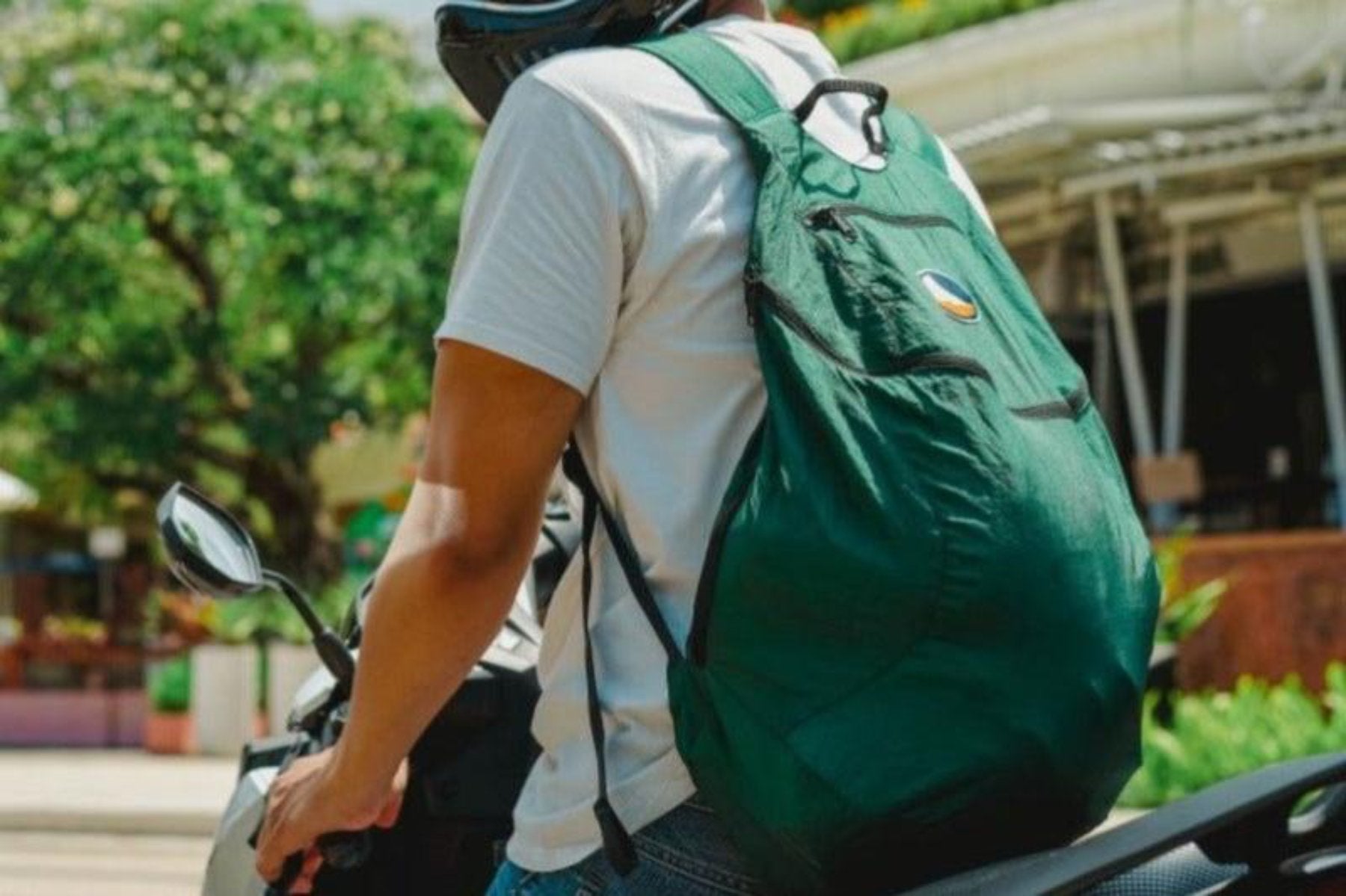 Grüner Backpack Plus von Ticket to the Moon auf dem Rücken einer Person mit Helm, die auf einem Motorrad sitzt – urbaner Einsatz im Alltag.