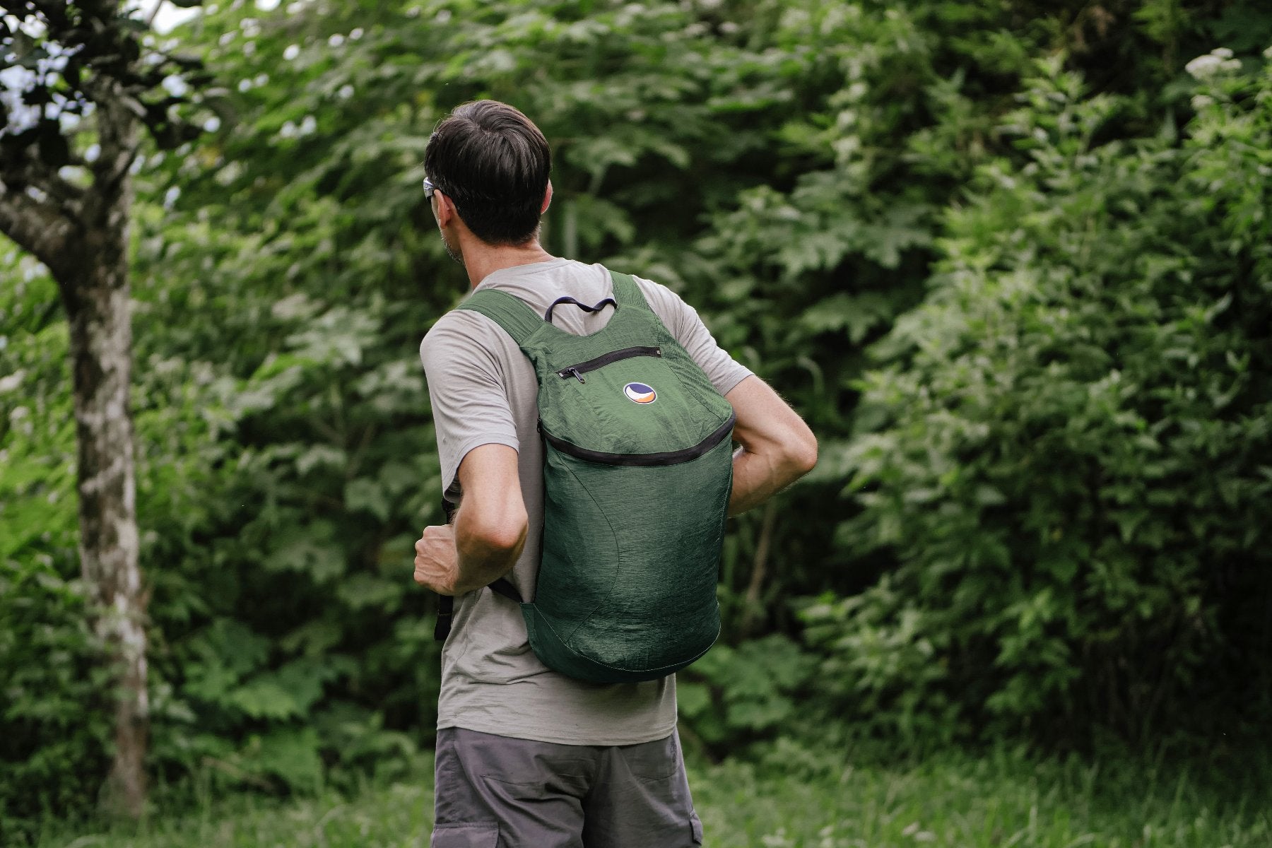Mann mit grünem Backpack Plus von Ticket to the Moon beim Wandern oder Spazieren in üppiger Natur, von hinten fotografiert.