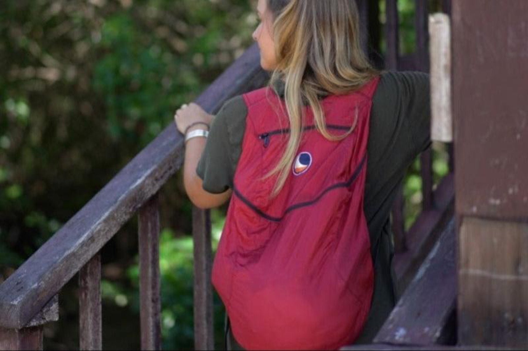 Frau mit rotem Backpack Plus von Ticket to the Moon auf einer Holztreppe im Wald, von hinten aufgenommen – praktischer Begleiter für Outdoor-Ausflüge.