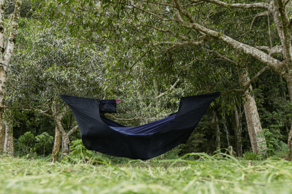 Hängematte mit gespanntem schwarzem 360° Mückennetz inmitten dichter Waldlandschaft, aufgehängt zwischen mehreren Bäumen auf einer Lichtung