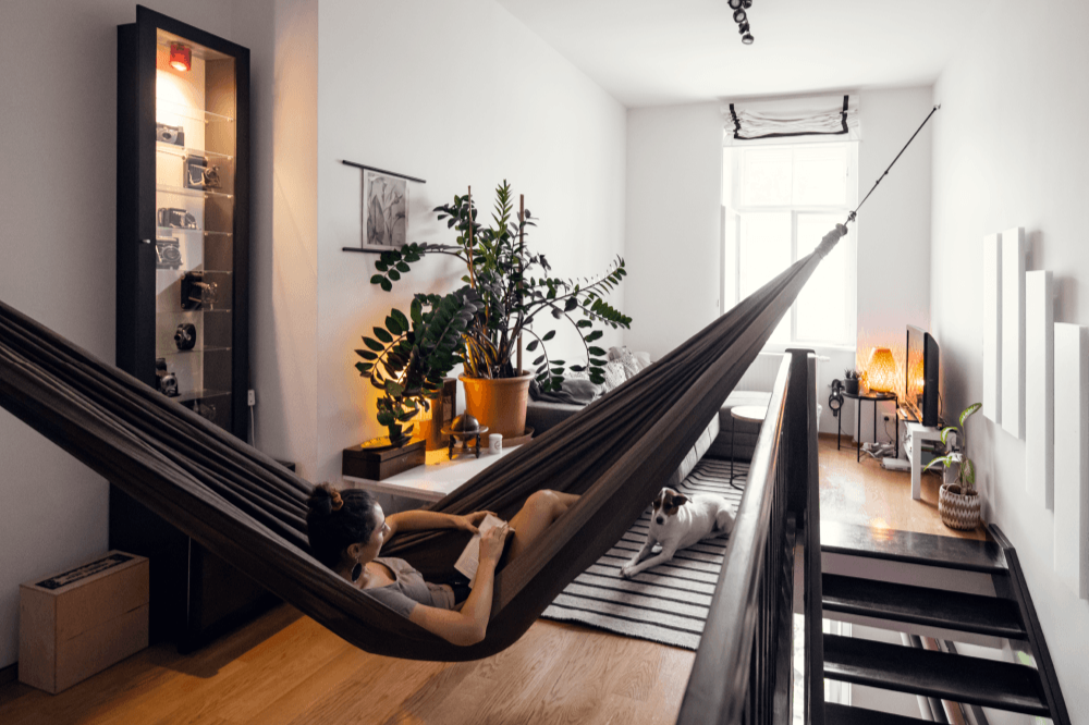 Frau liest in einer braunen Ticket to the Moon HOME HAMMOCK in einem modern eingerichteten Loft mit Hund auf dem Teppich.