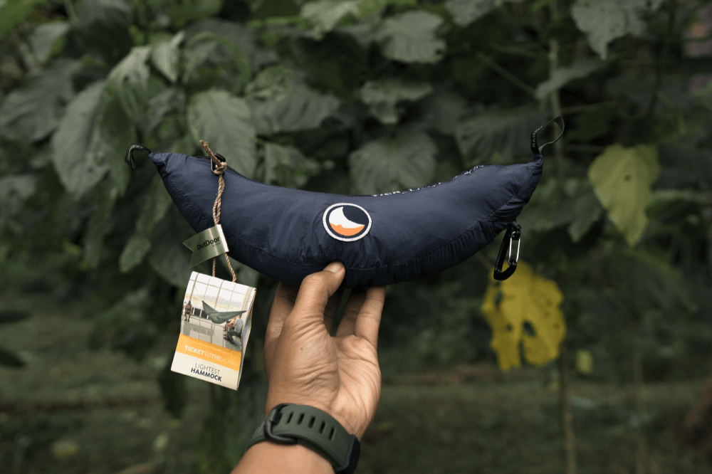 Die verpackte LIGHTEST HAMMOCK liegt auf der Hand in einem grünen Umfeld, mit einem Tag, der das Produkt und seine Verpackung zeigt.