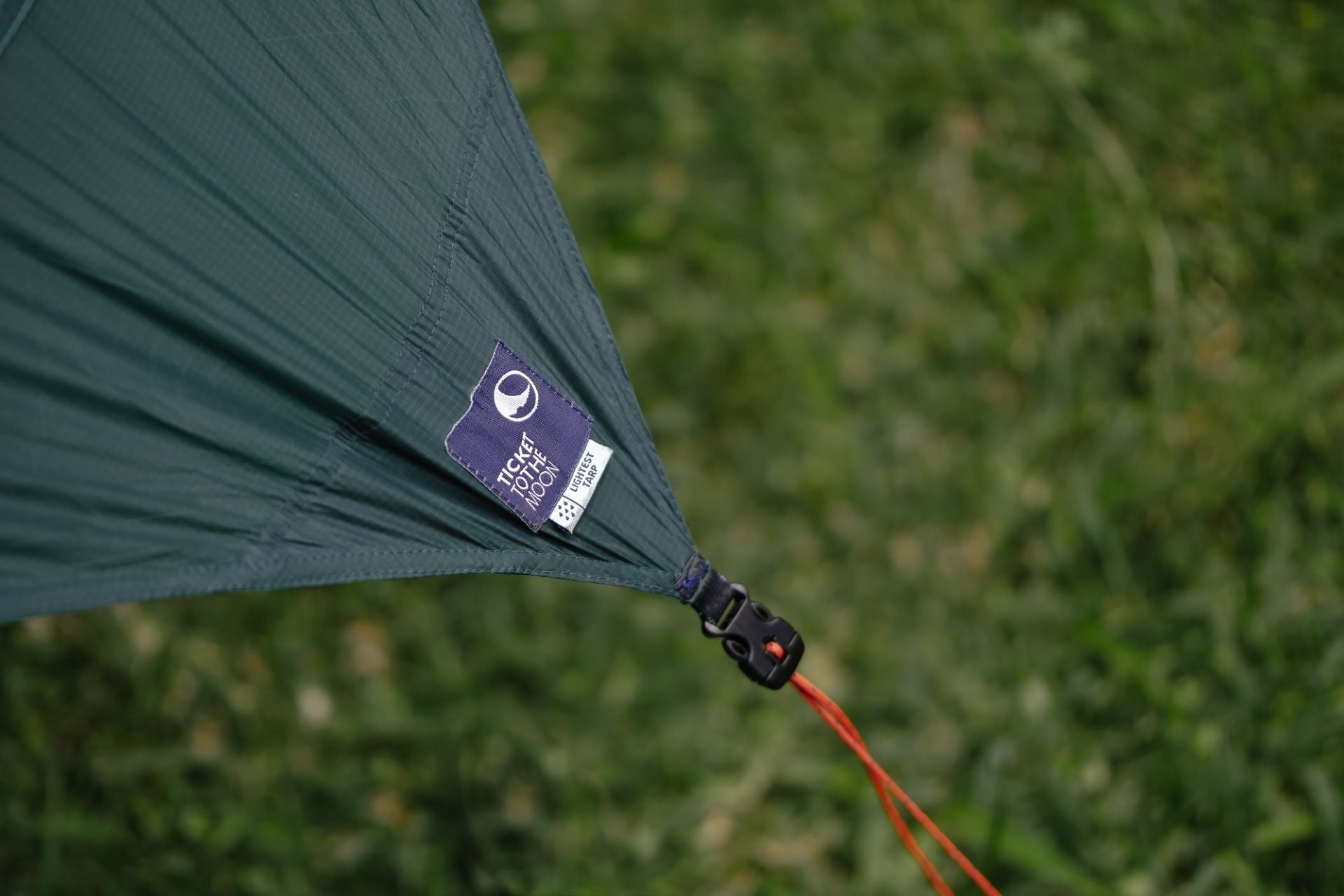 Detailaufnahme des LIGHTEST TARP: Label mit Logo und stabile Abspannschlaufe mit roter Leine auf grünem Hintergrund.