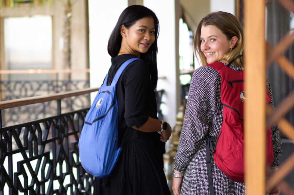 Zwei Frauen mit Mini Backpacks von Ticket to the Moon in Blau und Rot auf einem Balkon im urbanen Umfeld – stilvolle und leichte Begleiter für den Alltag.