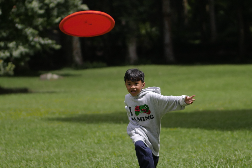Ein lachender Junge läuft über eine Wiese und fängt einen roten Moondisc in der Luft.
