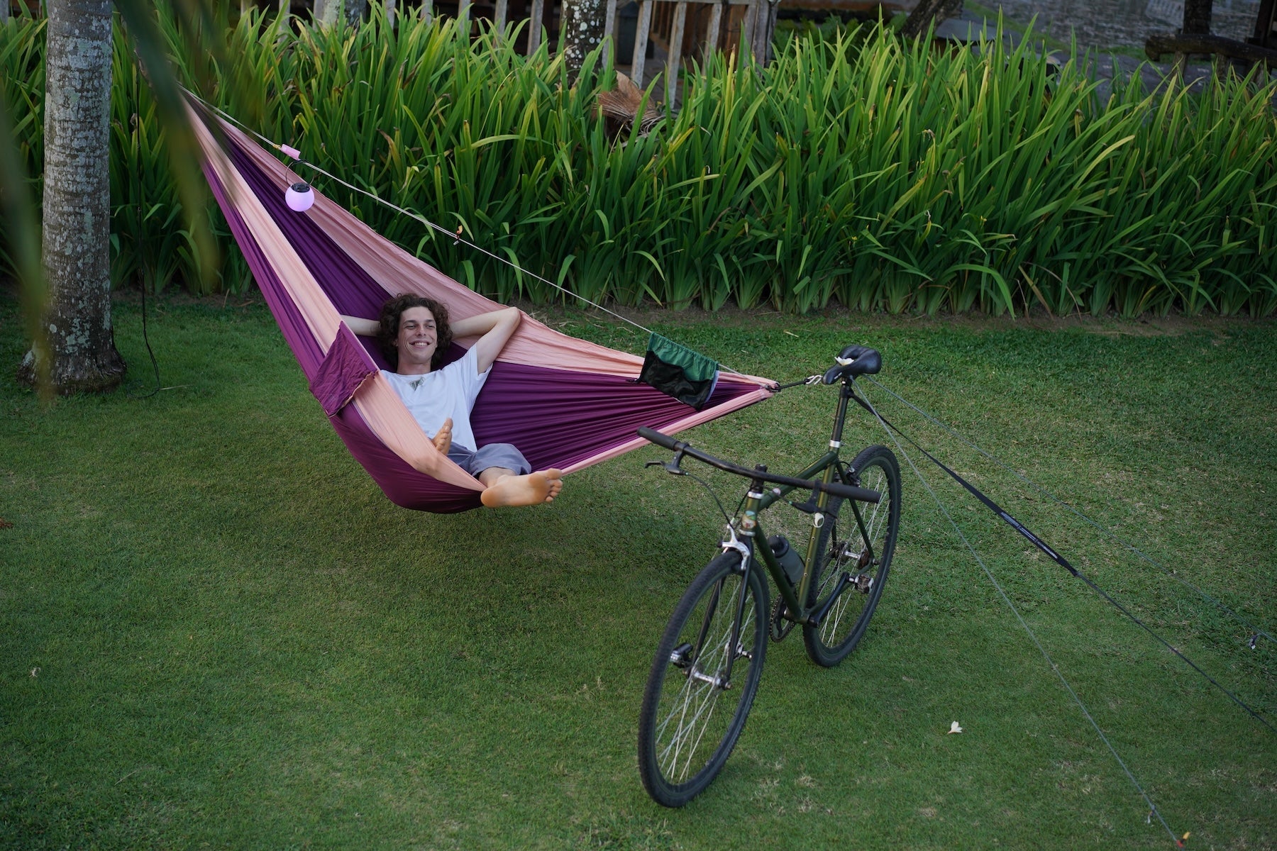 Hängematte ist mit einem 2nd Tree Kit an einem Fahrrad befestigt, eine Person liegt entspannt darin auf einer Wiese.