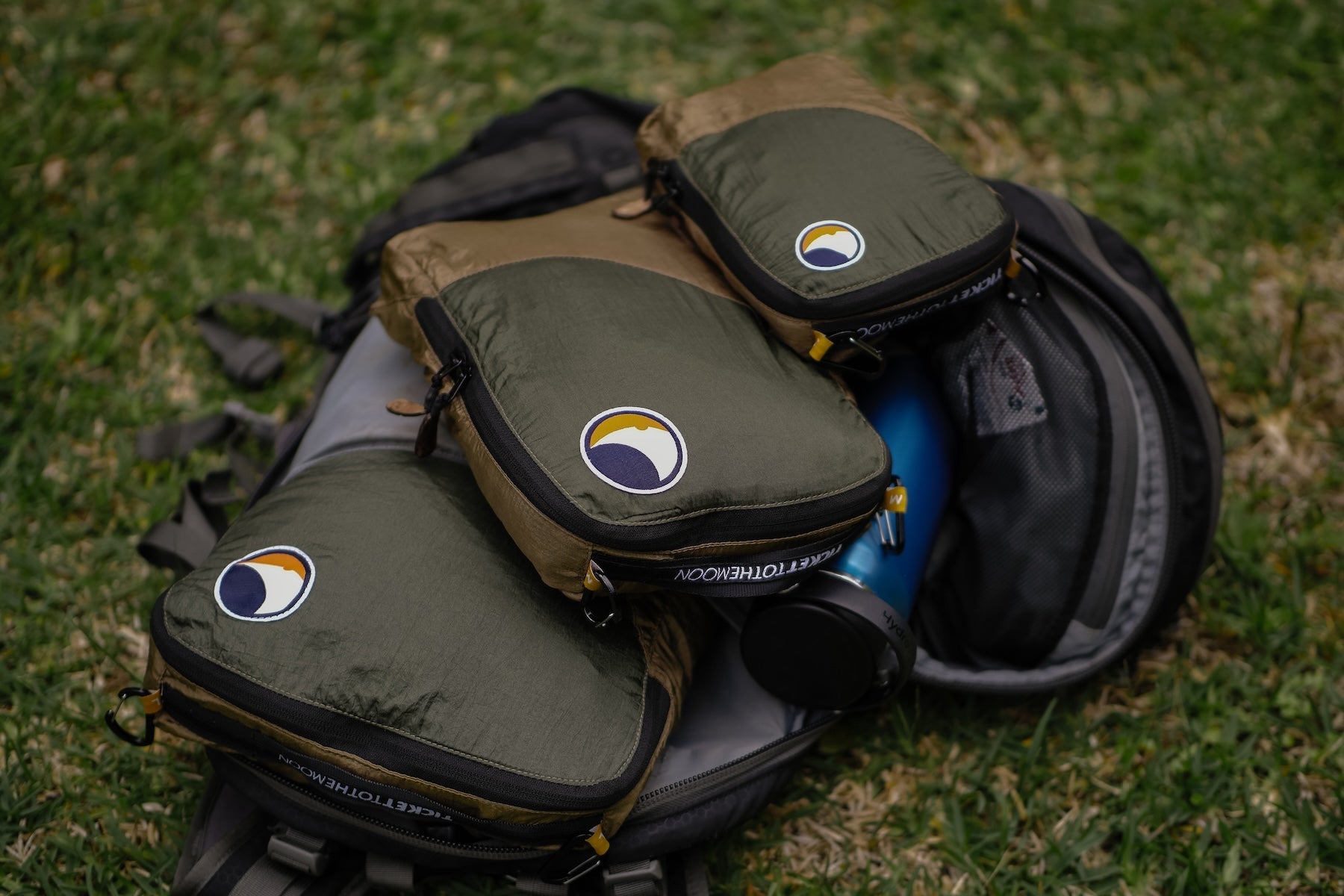 Drei olivgrüne Travel Cubes liegen ordentlich auf einem geöffneten Rucksack – ideal zum organisierten Packen auf Reisen.