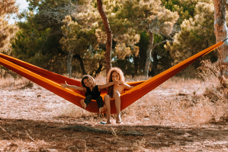 Zwei Kinder genießen gemeinsam die TRAVEL HAMMOCK Honeymoon in leuchtendem Orange – perfekte Hängematte für gemeinsame Outdoor-Momente.