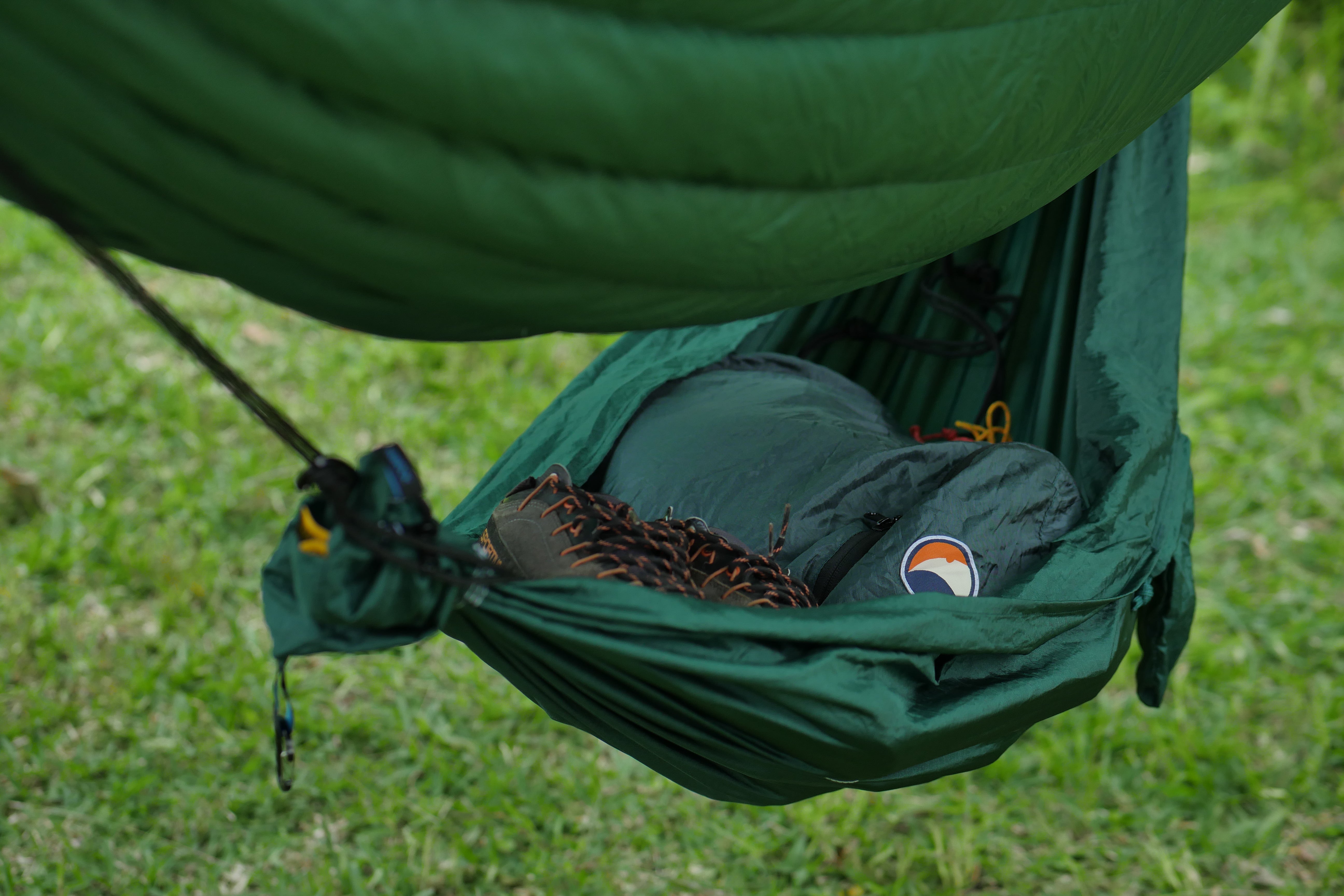 Eine Travel Hammock Mini von Ticket to the Moon wird als Gearbag verwendet und hängt aufgespannt unter einer großen Hängematte. In der Mini Hängematte befinden sich ein Rucksack, Schuhe und Seile.