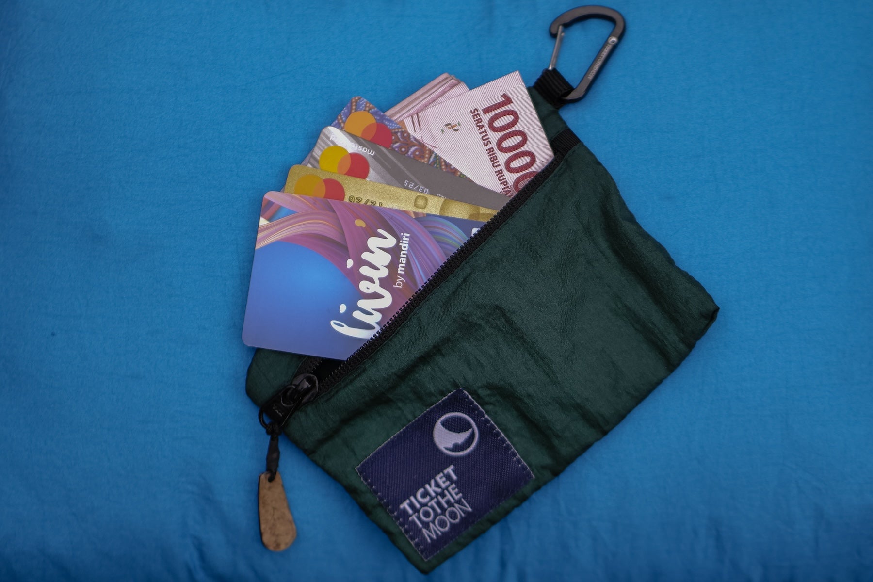 Grünes Travel Wallet von Ticket to the Moon mit Geldscheinen und Karten auf blauem Hintergrund