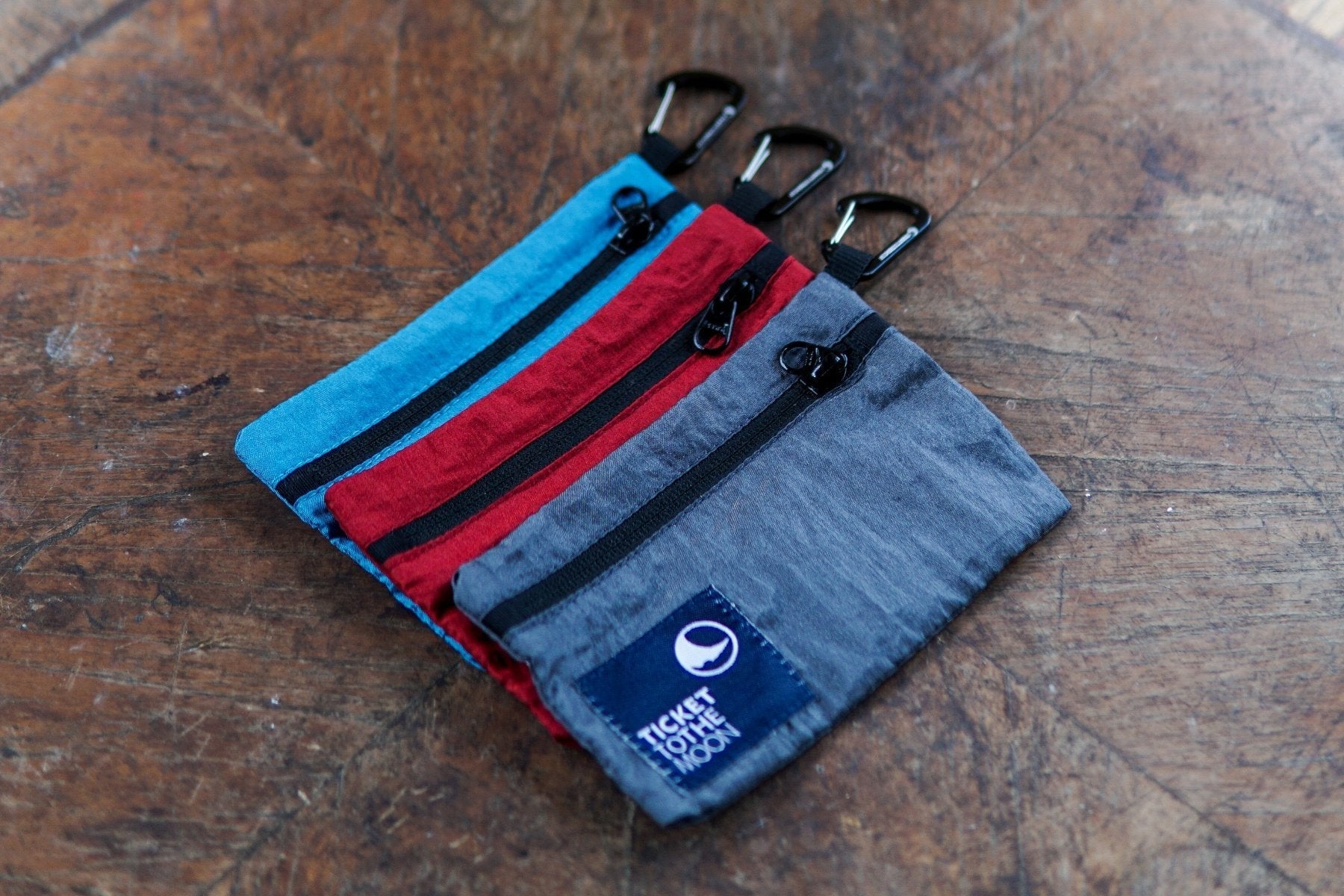 Travel Wallets von Ticket to the Moon in Blau, Rot und Grau mit Karabinern auf Holztisch