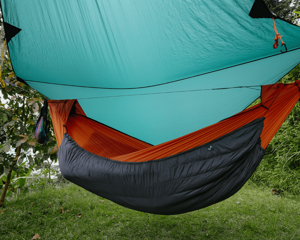 Komplettes Hängematten-Setup von TTTM mit orangefarbener Hängematte, schwarzem Underquilt und türkisfarbenem Tarp – Outdoor-Aufbau auf Wiese