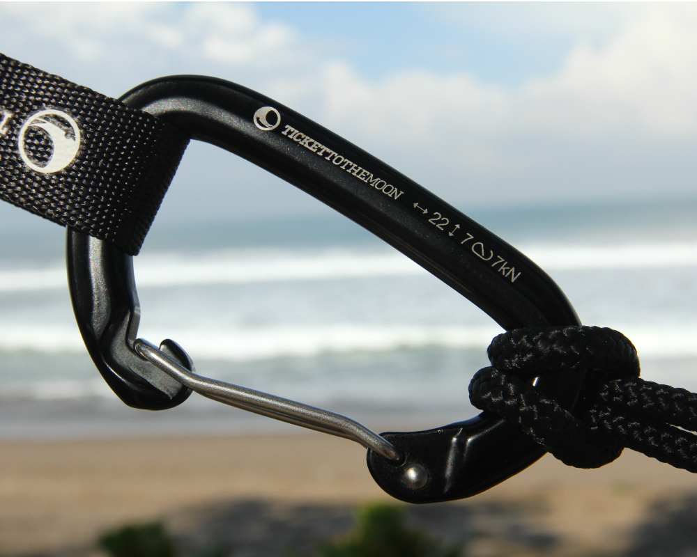 Nahaufnahme des TTTM Karabiners mit 22 kN Bruchlast – befestigt mit Gurtband und Seil, im Hintergrund das Meer