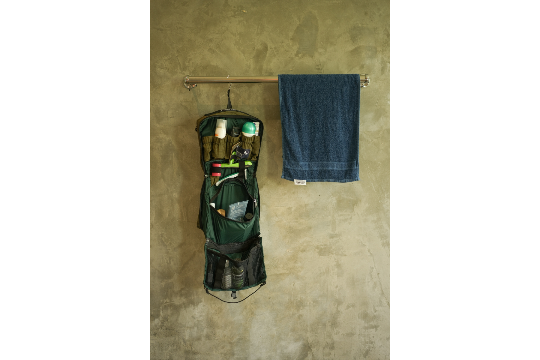 Befüllte Washbag von Ticket to the Moon, offen und an einer Stange neben einem Handtuch aufgehängt – mit praktischen Fächern für Hygieneartikel wie Zahnbürste, Shampoo und Sonnencreme.