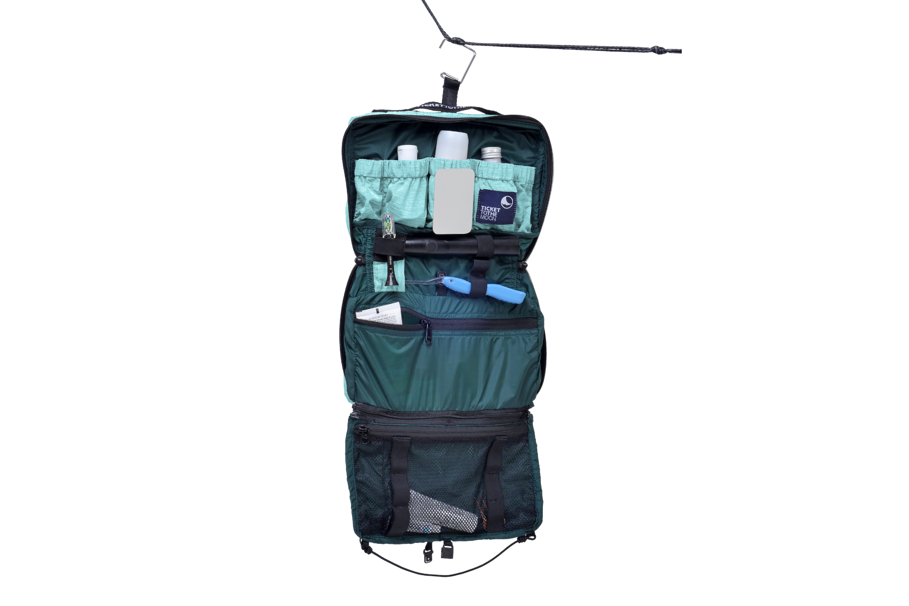 Geöffnete und befüllte türkise Washbag von Ticket to the Moon, aufgehängt an einer Schnur – mit Fläschchen, Spiegel, Werkzeug und Zahnbürste, ideal organisiert für Reisen und Camping.