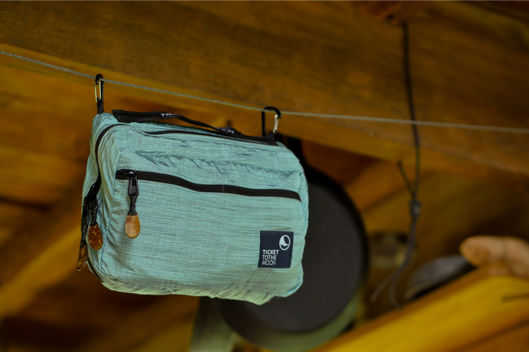 Geschlossene türkisfarbene Washbag von Ticket to the Moon mit Holz-Zippern, an einer Leine unter einem Holzdach aufgehängt – ideal für Camping und Reisen mit Stil.