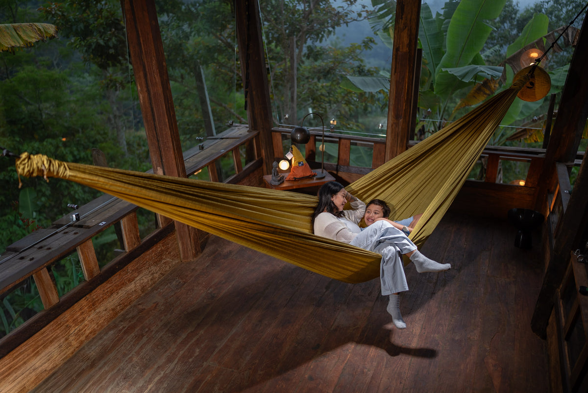 Mutter und Kind entspannen in einer goldenen Home Hammock 420 auf einer Holzterrasse mitten im Dschungel