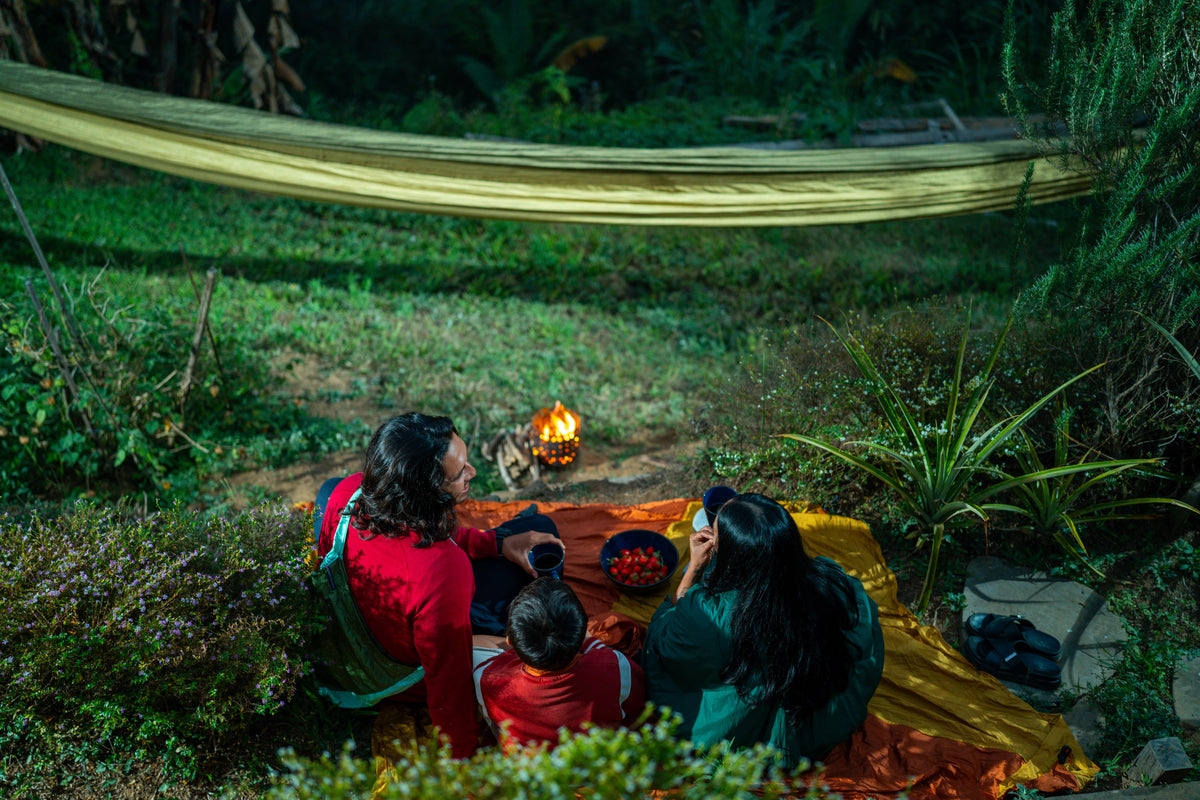 Familie sitzt in der Dämmerung auf einer Picknickdecke an einem kleinen Lagerfeuer unter einer goldenen Home Hammock 520