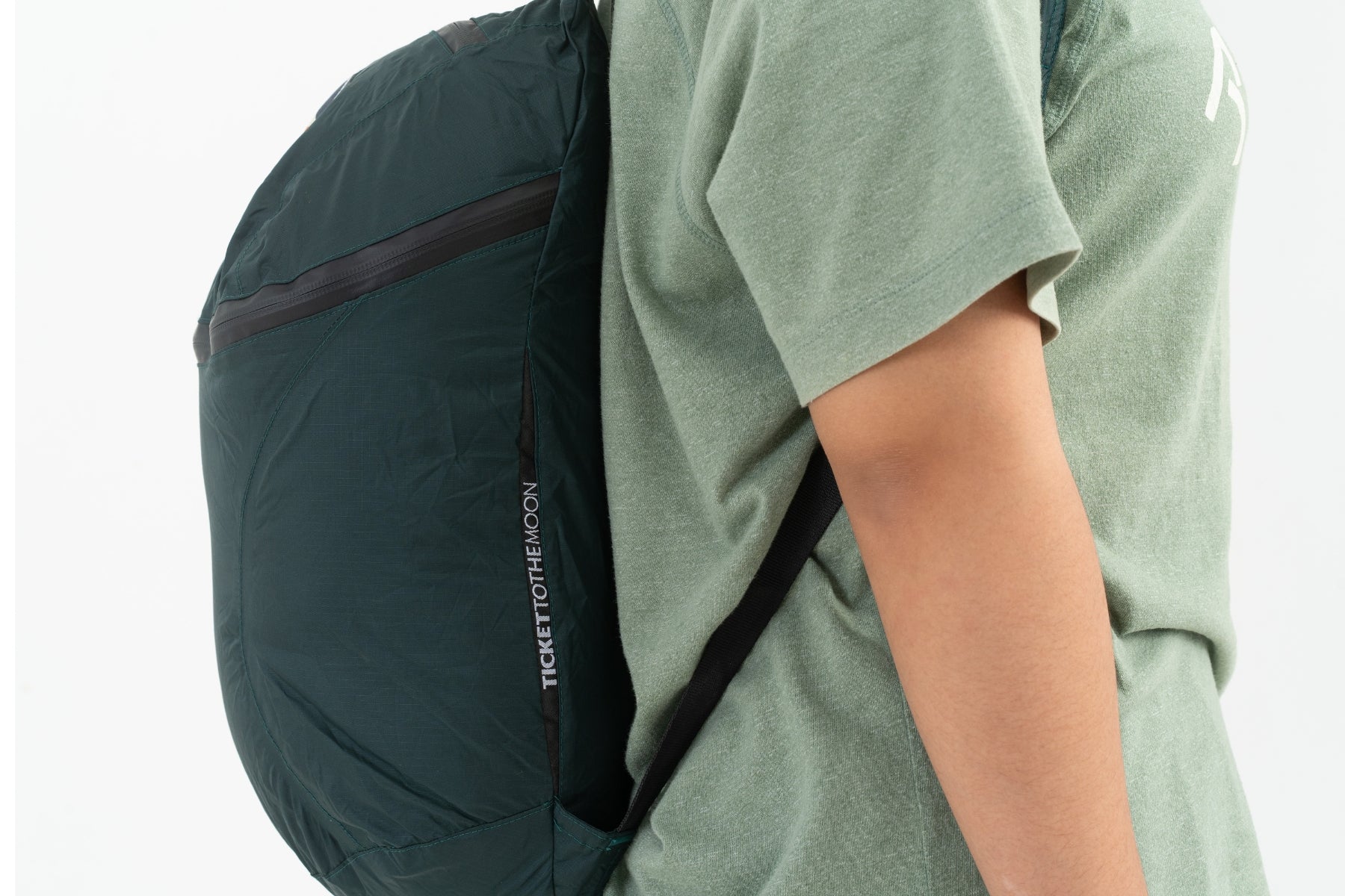 Seitenansicht des dunkelgrünen Ticket to the Moon Mini Backpacks, getragen von einer Person. Gut sichtbar sind der wassergeschützte Reißverschluss des Top-Fachs und das vertikale Marken-Logo-Patch an der Seite.