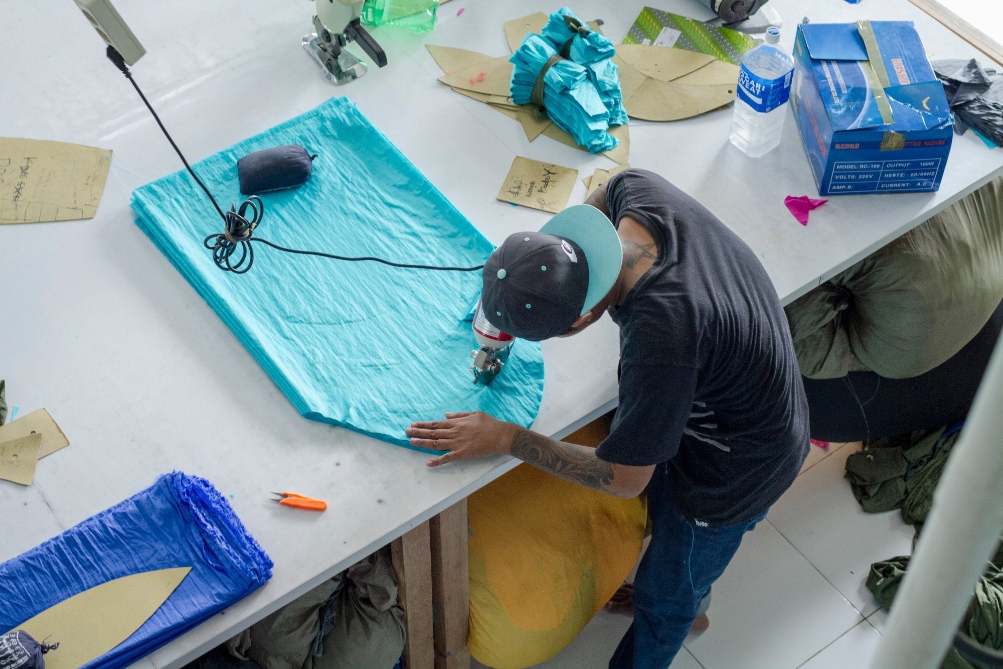 Mitarbeiter schneidet blauen Stoff sorgfältig per Hand im Upcycling-Workshop in Bali
