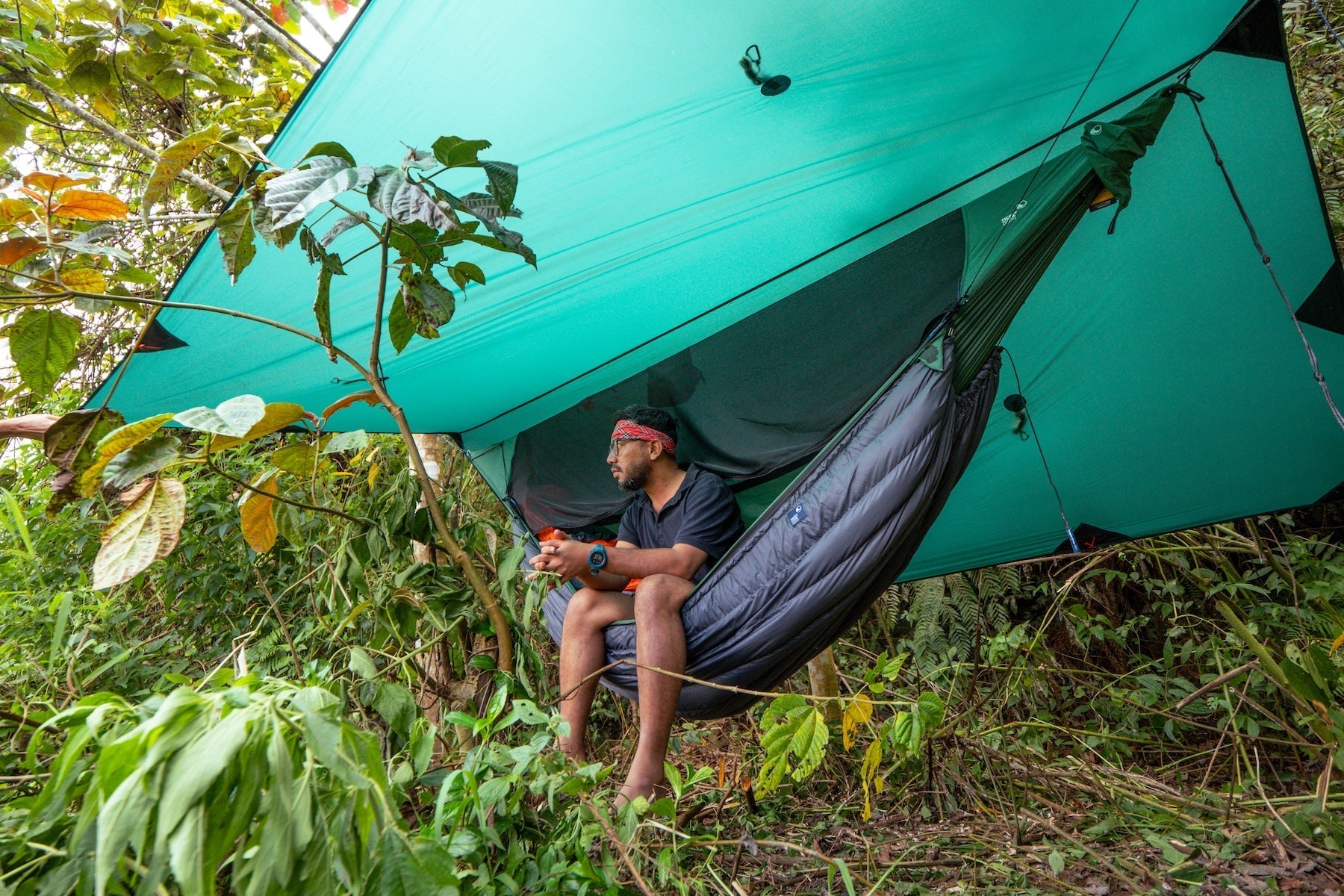 Mann entspannt unter dem FULLMOON TARP in einer Hängematte mit Isolationsquilt – vielseitiger Allwetterschutz aus recyceltem Sil-Nylon für Wind und Regen.