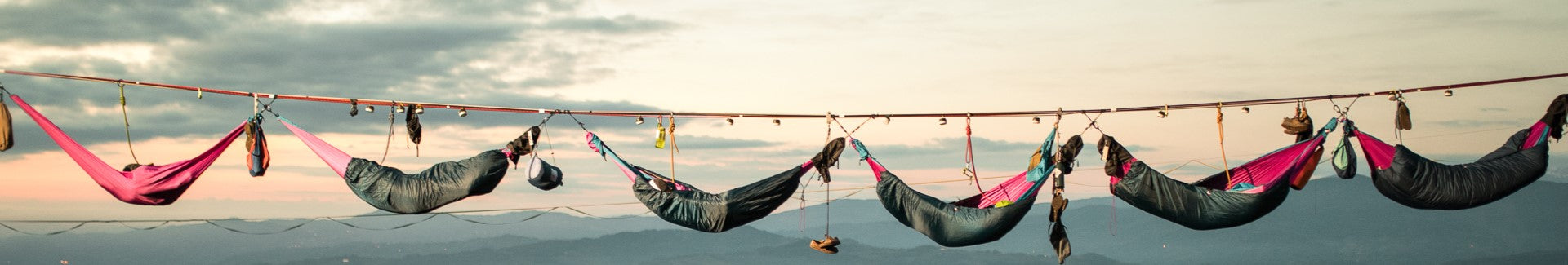 Mehrere Hängematten hängen spektakulär über einer Highline bei Sonnenuntergang mit Blick auf Berge und Himmel