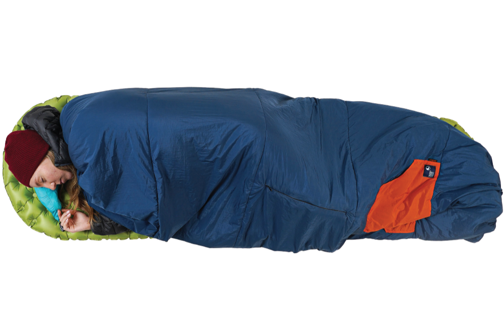 Person liegt schlafend seitlich eingerollt in der geschlossenen Moonblanket auf einer grünen Isomatte, dunkelblaue Decke mit orangefarbener Tasche gut sichtbar