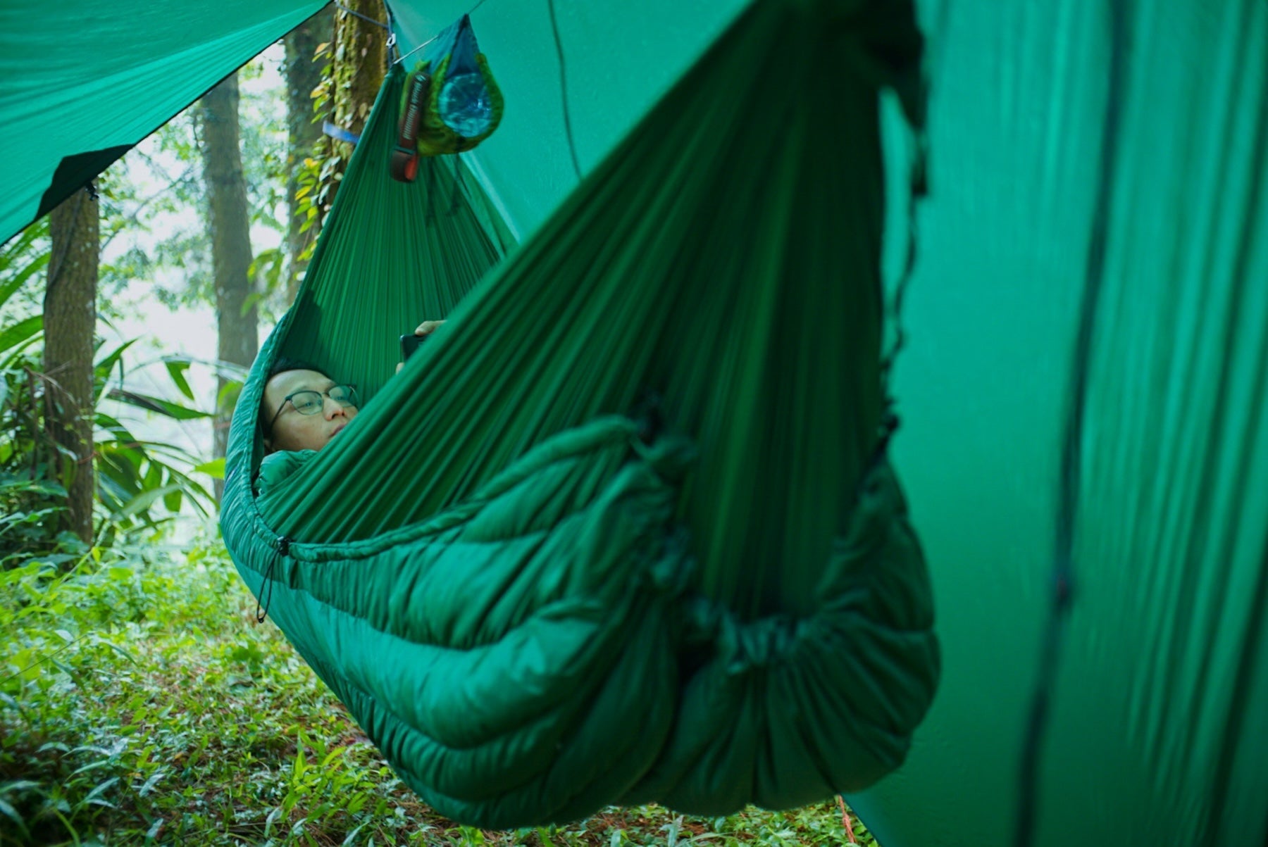 Person liegt entspannt mit dem MoonQuilt Pro 850 in einer Hängematte im Wald – perfekter Schutz vor Kälte beim Outdoor-Camping.