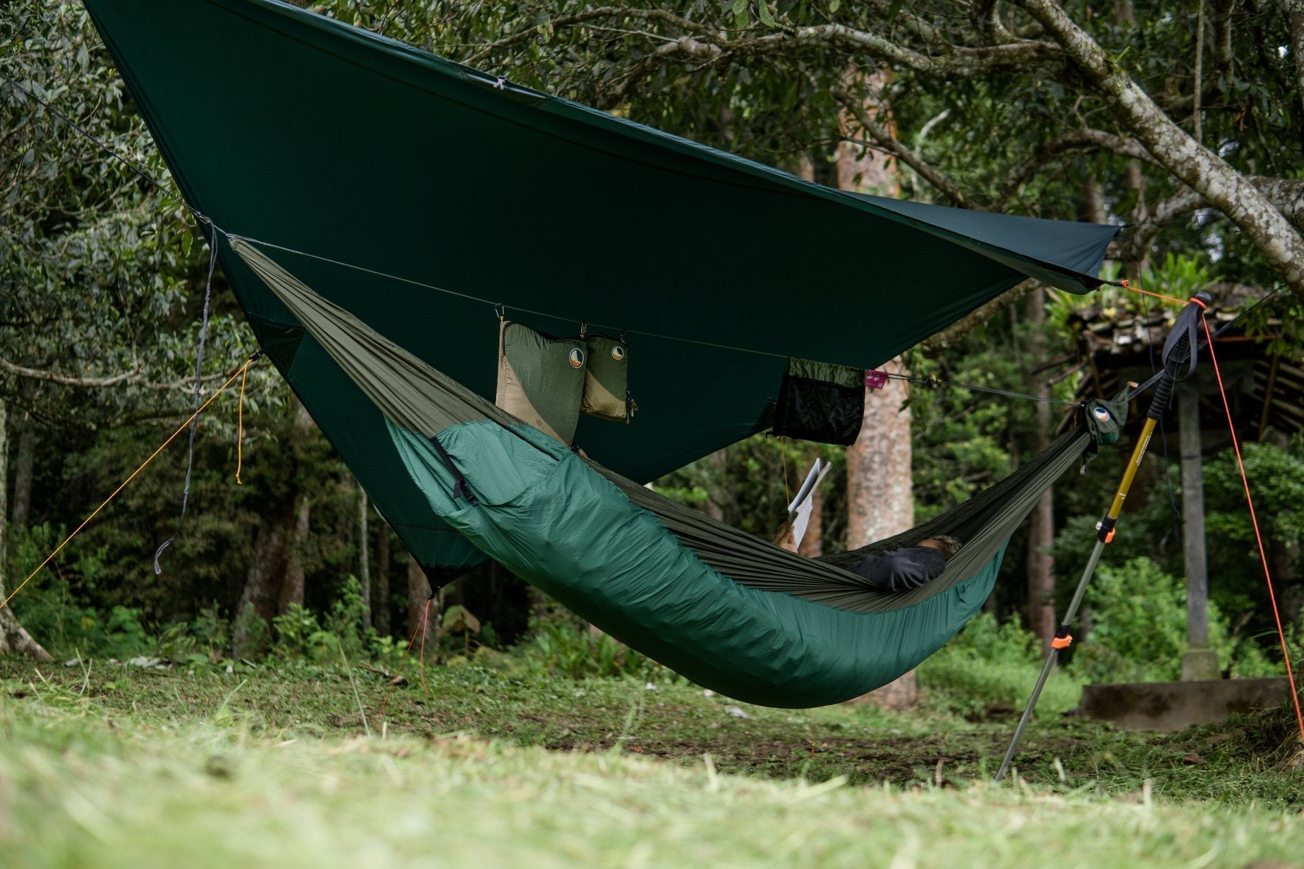 Camping-Setup mit grünem Moontarp, Hängematte mit Underquilt und organisiertem Zubehör in der Ridgeline-Tasche.