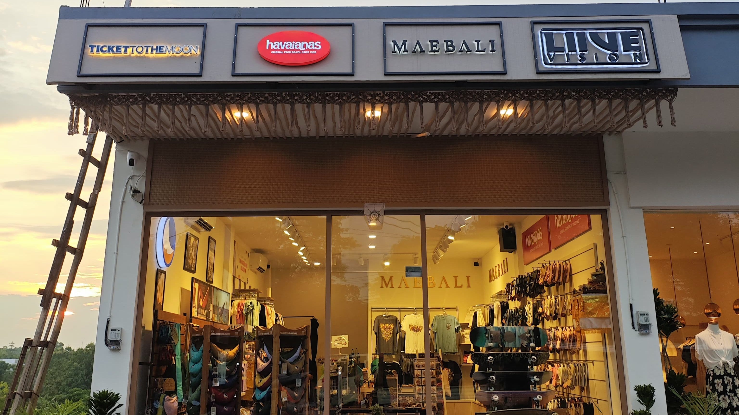 Ladenfassade in Bali/Uluwatu mit den Marken Ticket to the Moon, Havaianas, Maebali und Live Vision – Blick ins Geschäft mit Hängematten, Kleidung und Accessoires im Sonnenuntergang.