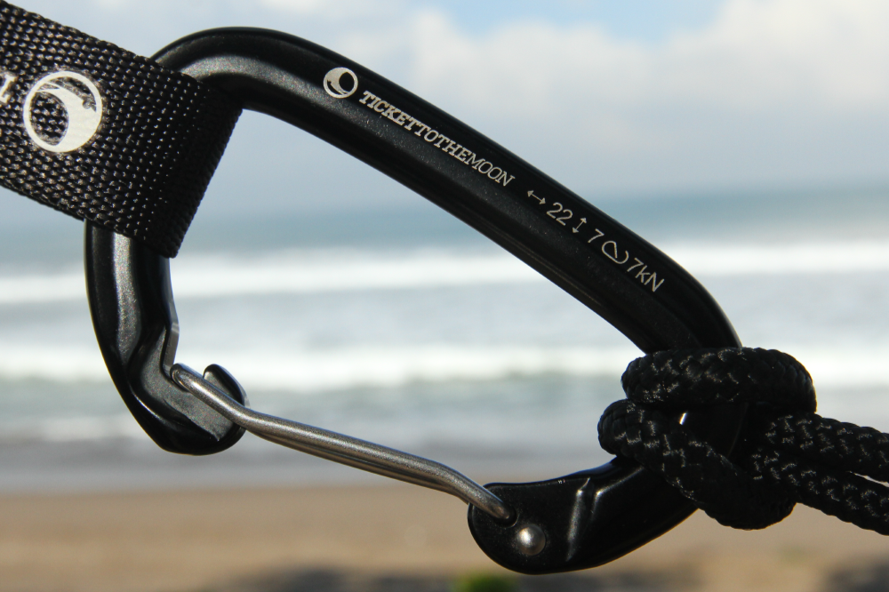 Nahaufnahme des TTTM Karabiners mit 22 kN Bruchlast – befestigt mit Gurtband und Seil, im Hintergrund das Meer