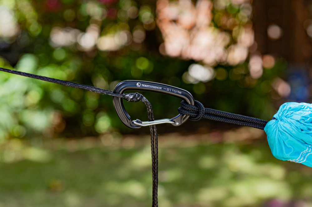 TTTM Karabiner sichert eine Hängematte im Garten – verbunden mit schwarzem Seil und Seesack-Knoten, ideal für entspannte Outdoor-Momente