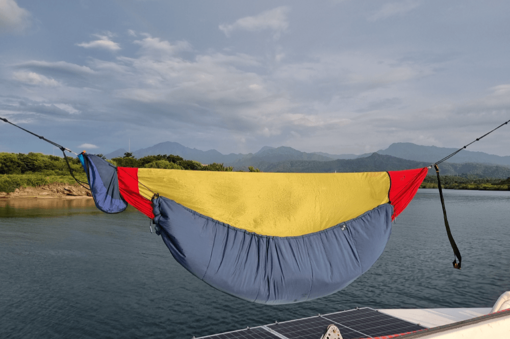 TTTM Hängematte mit Underquilt auf einem Boot – aufgehängt über dem Wasser mit Bergpanorama im Hintergrund