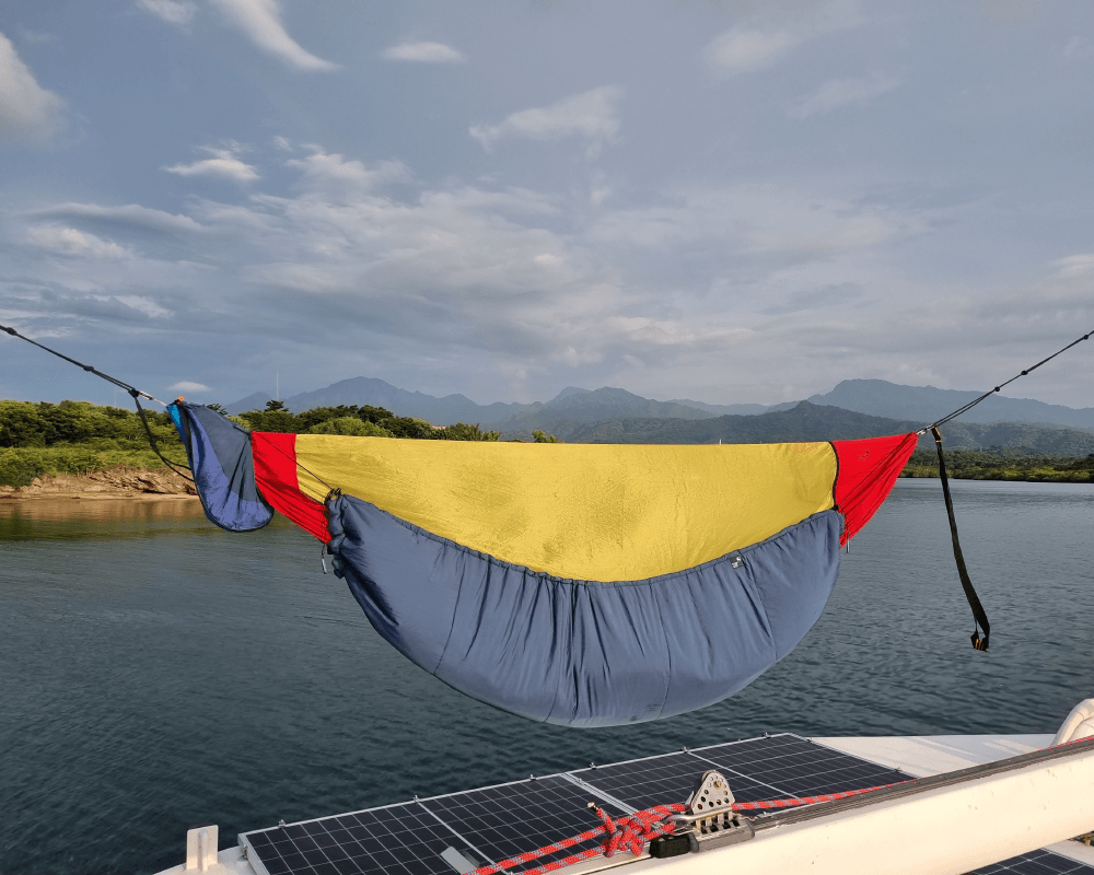 TTTM Hängematte mit buntem Underquilt auf einem Boot – aufgehängt über dem Wasser mit Bergpanorama im Hintergrund