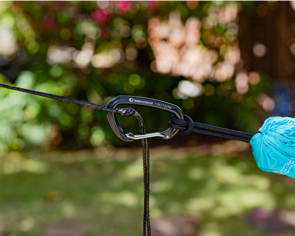 TTTM Karabiner sichert eine Hängematte im Garten – verbunden mit schwarzem Seil und Seesack-Knoten, ideal für entspannte Outdoor-Momente