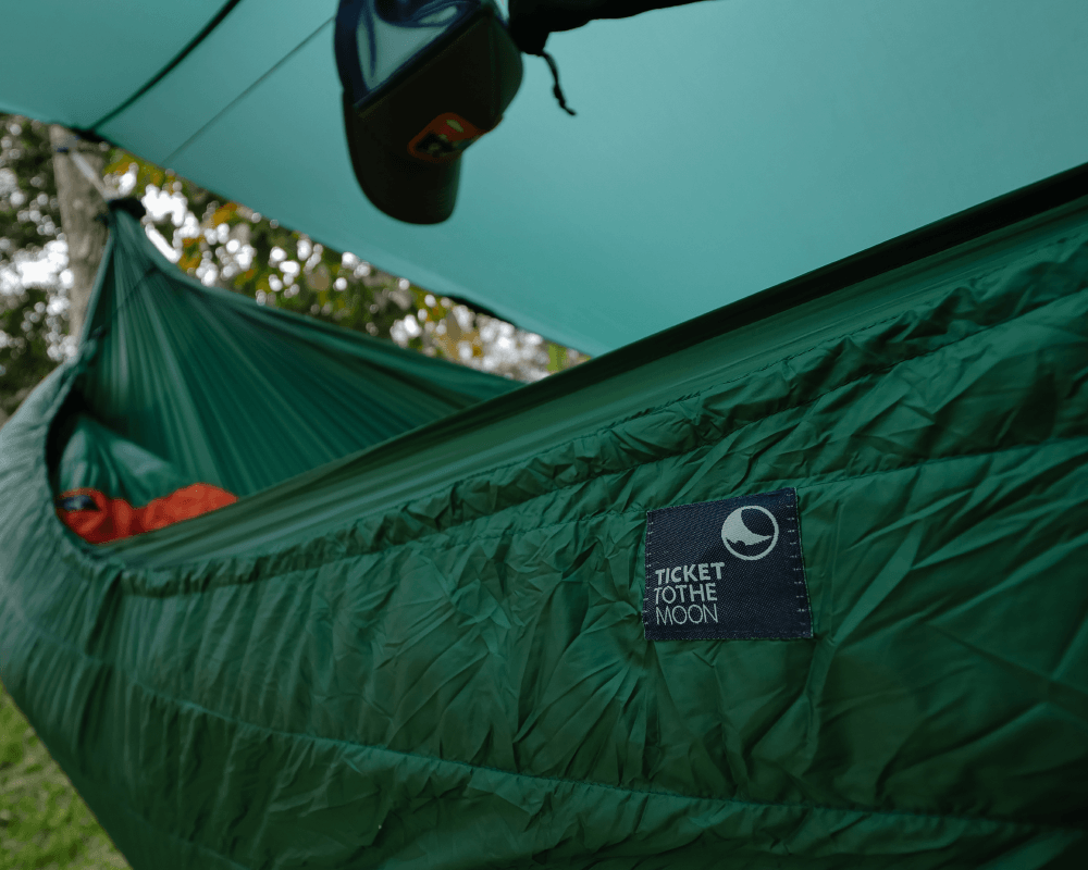 Detailaufnahme des grünen TTTM Underquilts im Outdoor-Einsatz – mit Hängematte und Tarp für maximalen Komfort beim Camping